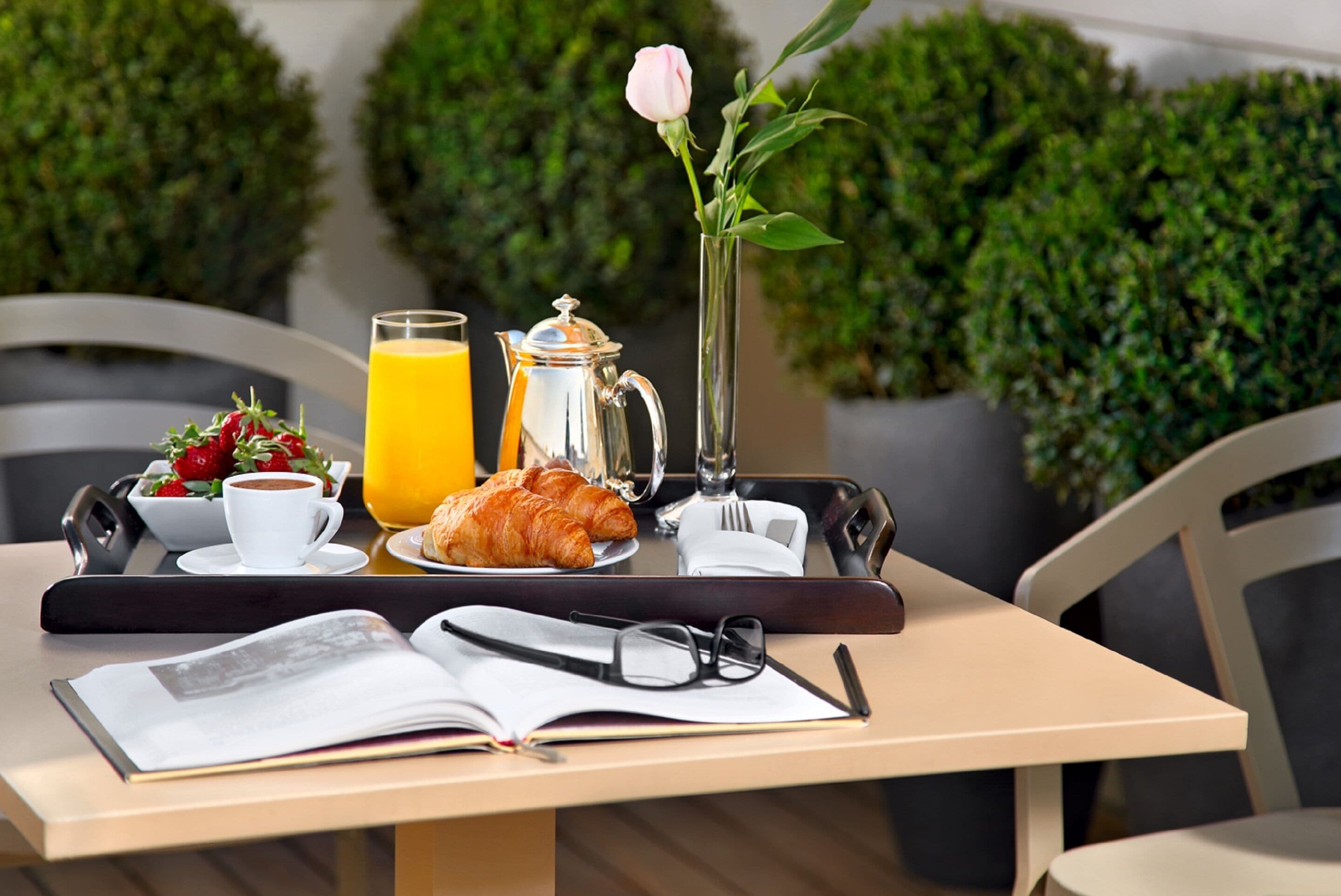 Een ontbijtje met croissants, koffie, sinaasappelsap en een roos in een vaas op een tafel.