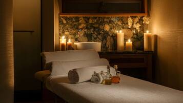 A spa room with a massage table, candles, and a decorative wall.