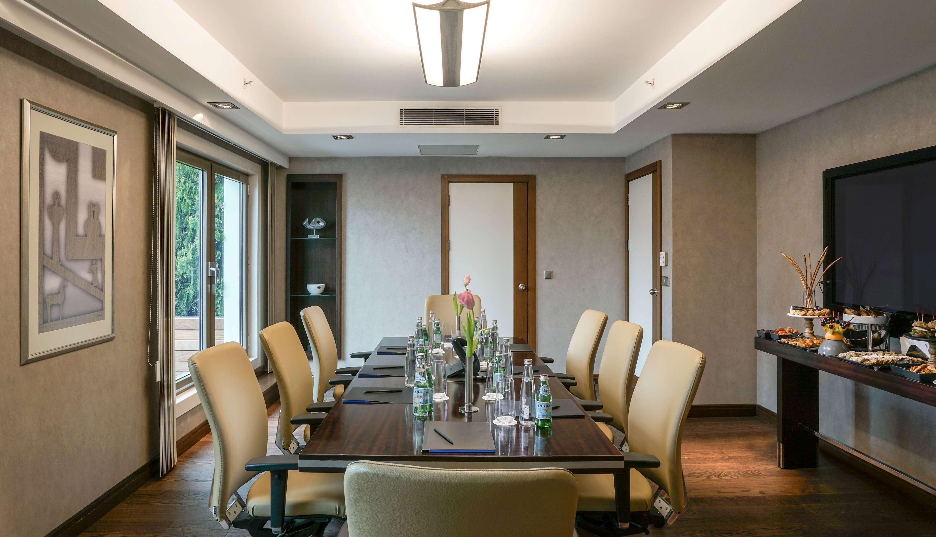 A conference room with a long table, chairs, a vase with a flower, and a buffet table with snacks.