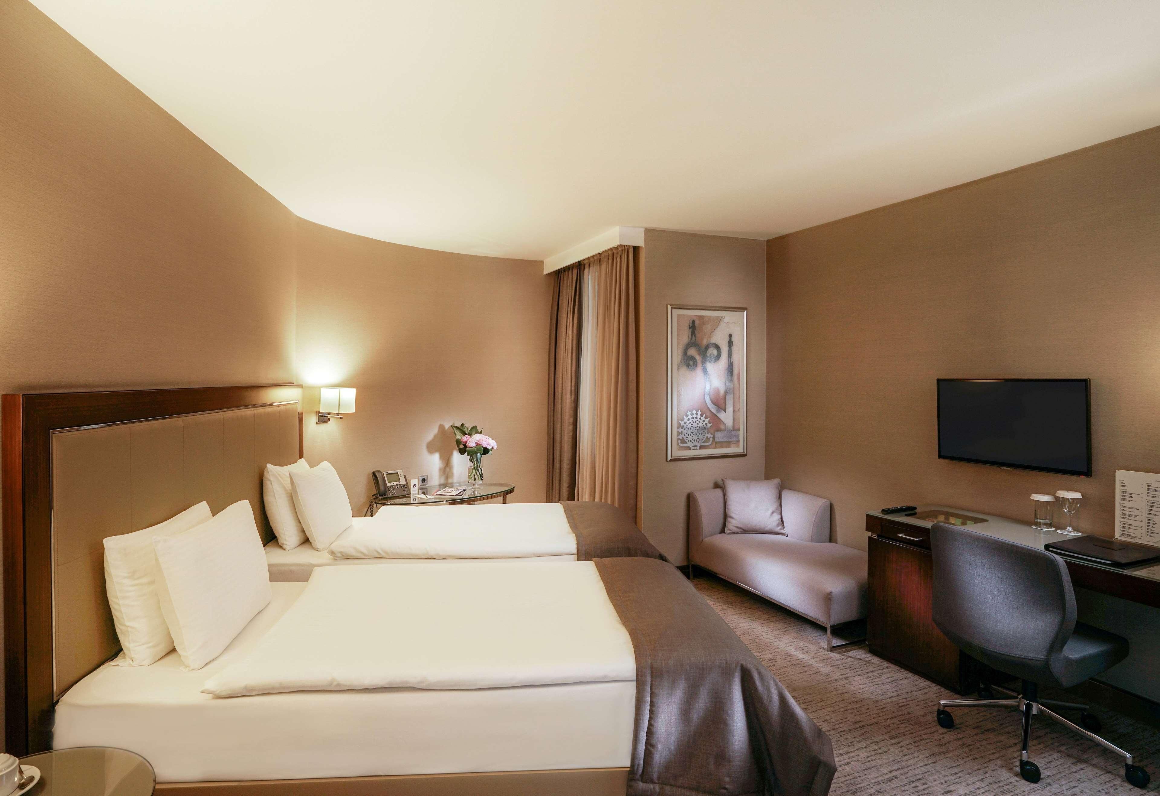 Une chambre d’hôtel avec deux lits, un bureau, une chaise, une télévision et un téléphone fixé au mur.