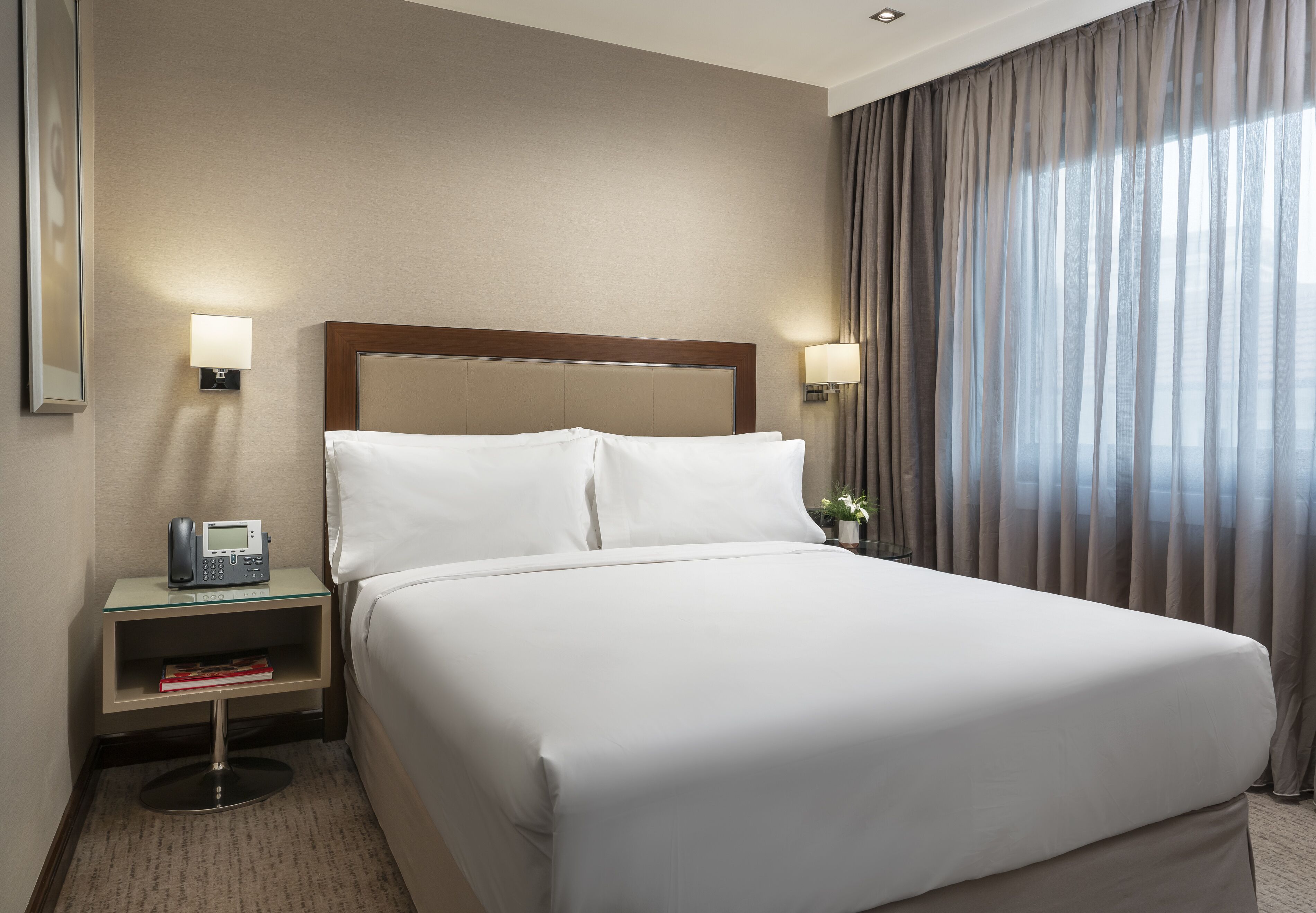 Una habitación de hotel con una cama grande, dos mesitas de noche, un teléfono y una lámpara.