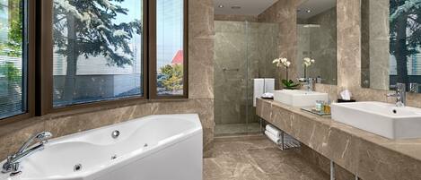 A modern bathroom with a large bathtub, two sinks, and a walk-in shower.