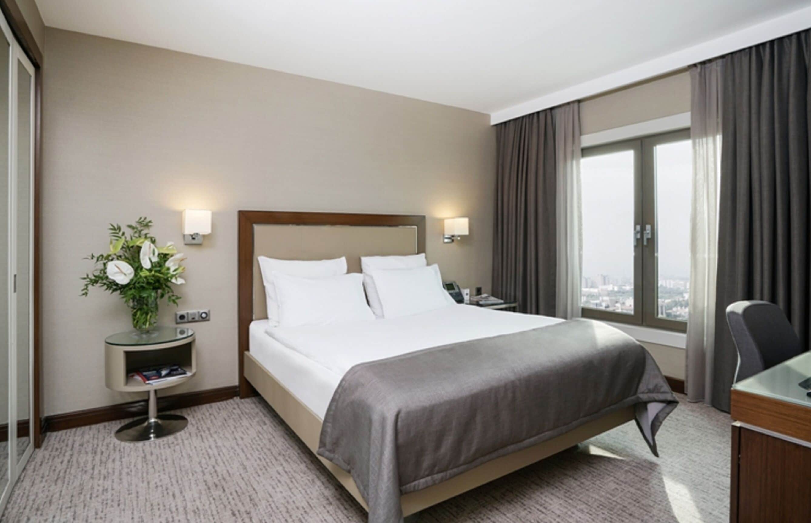 Una habitación de hotel con una cama grande, mesitas de noche, un escritorio y una ventana con cortinas.