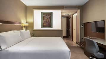 Ein Hotelzimmer mit einem großen Bett, einem Schreibtisch mit Stuhl, einem Fernseher und einem Wandbild.