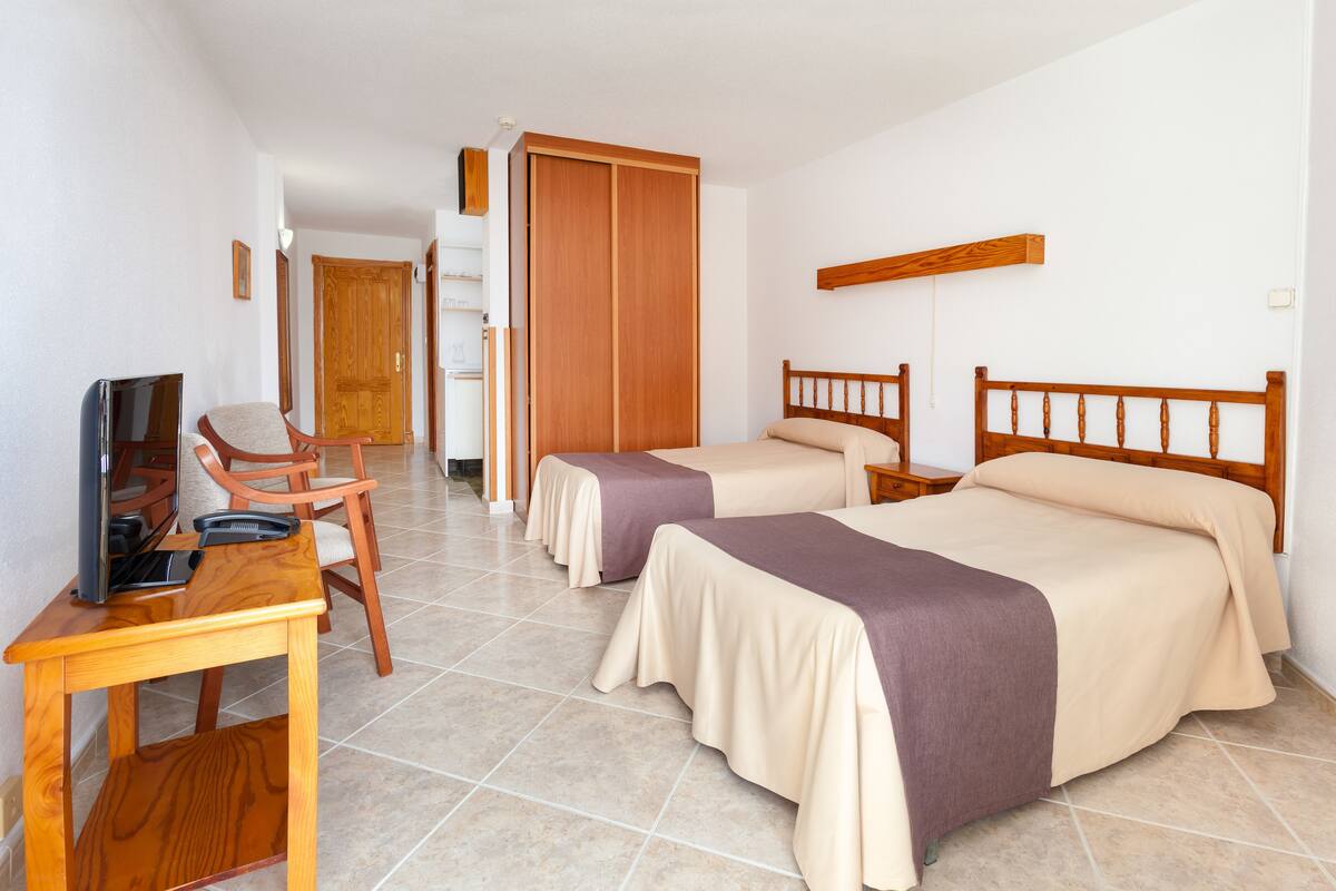 Une chambre d’hôtel avec deux lits, un bureau avec un ordinateur et une télévision.