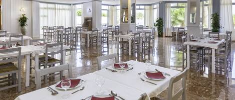 Un comedor espacioso con varias mesas dispuestas para comer, grandes ventanales que dejan entrar luz natural y un suelo de mármol pulido.