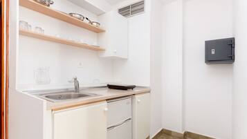 A compact kitchen with a sink, countertop, and built-in oven. There is a small refrigerator and a wall-mounted safe.