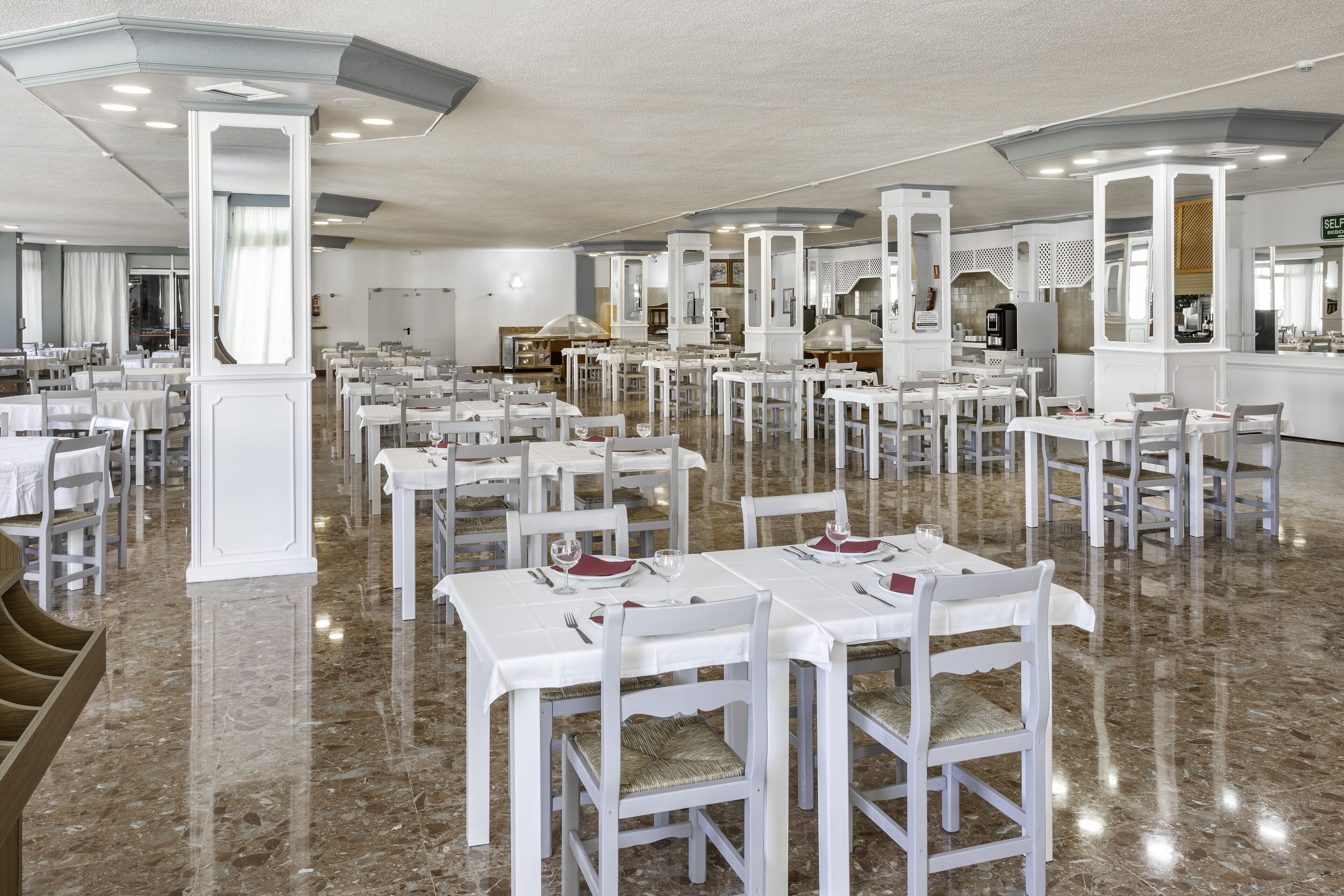 A spacious restaurant with white tables and chairs, marble flooring, and a modern interior design.