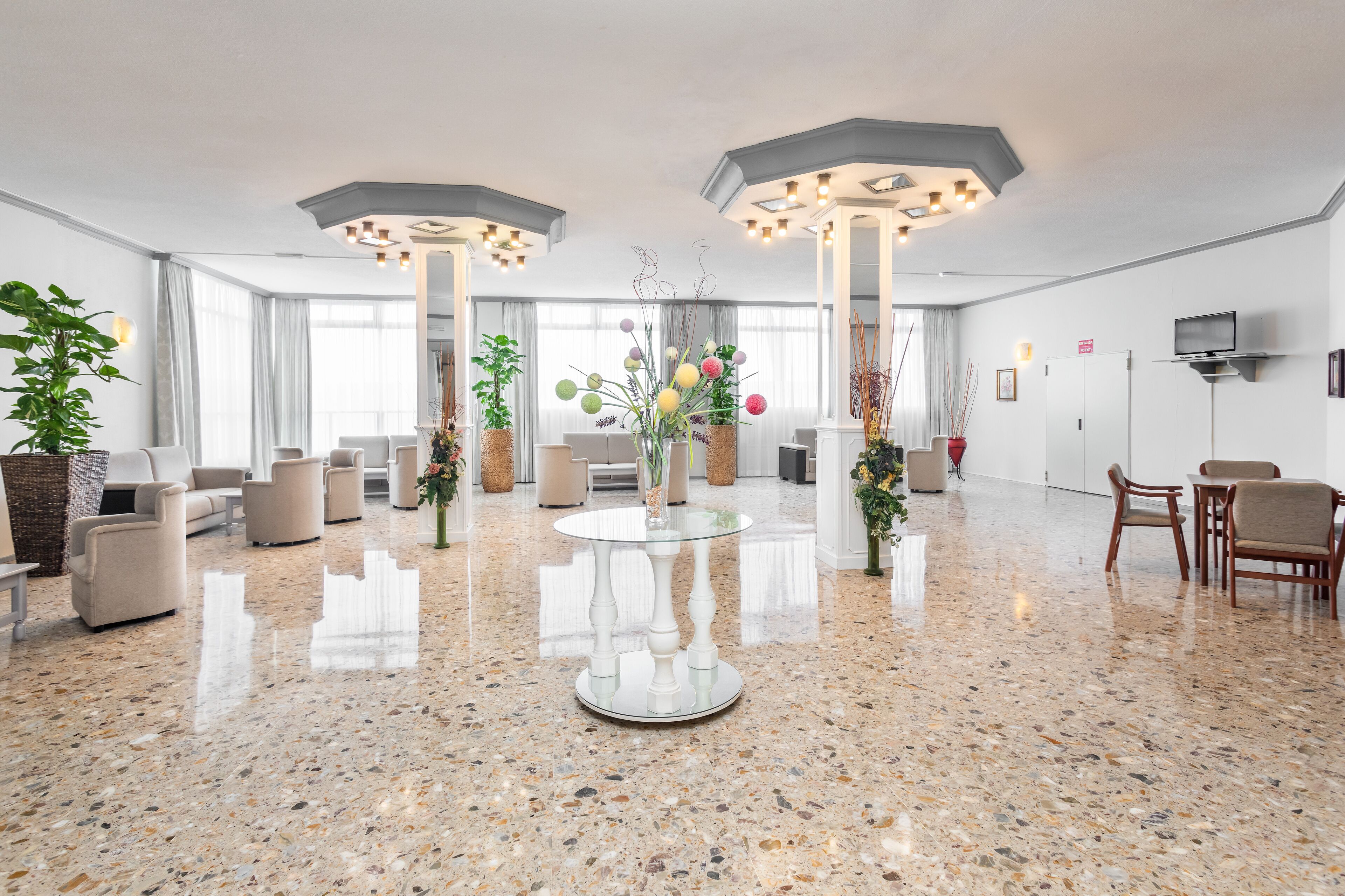 A spacious lobby with a polished granite floor, comfortable seating, and a central glass table.