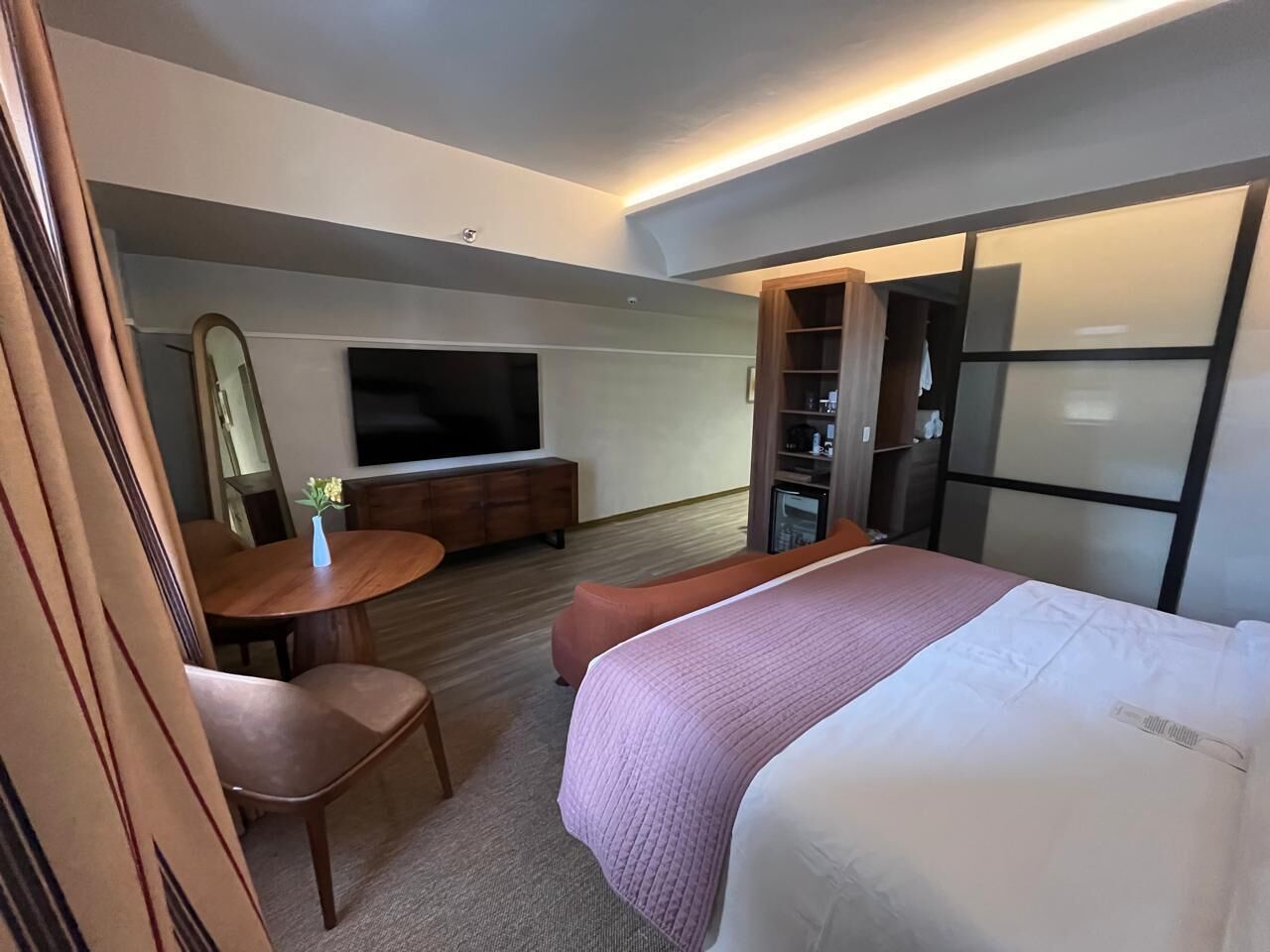 A hotel room with a bed, a desk, a chair, a TV, and a wardrobe.