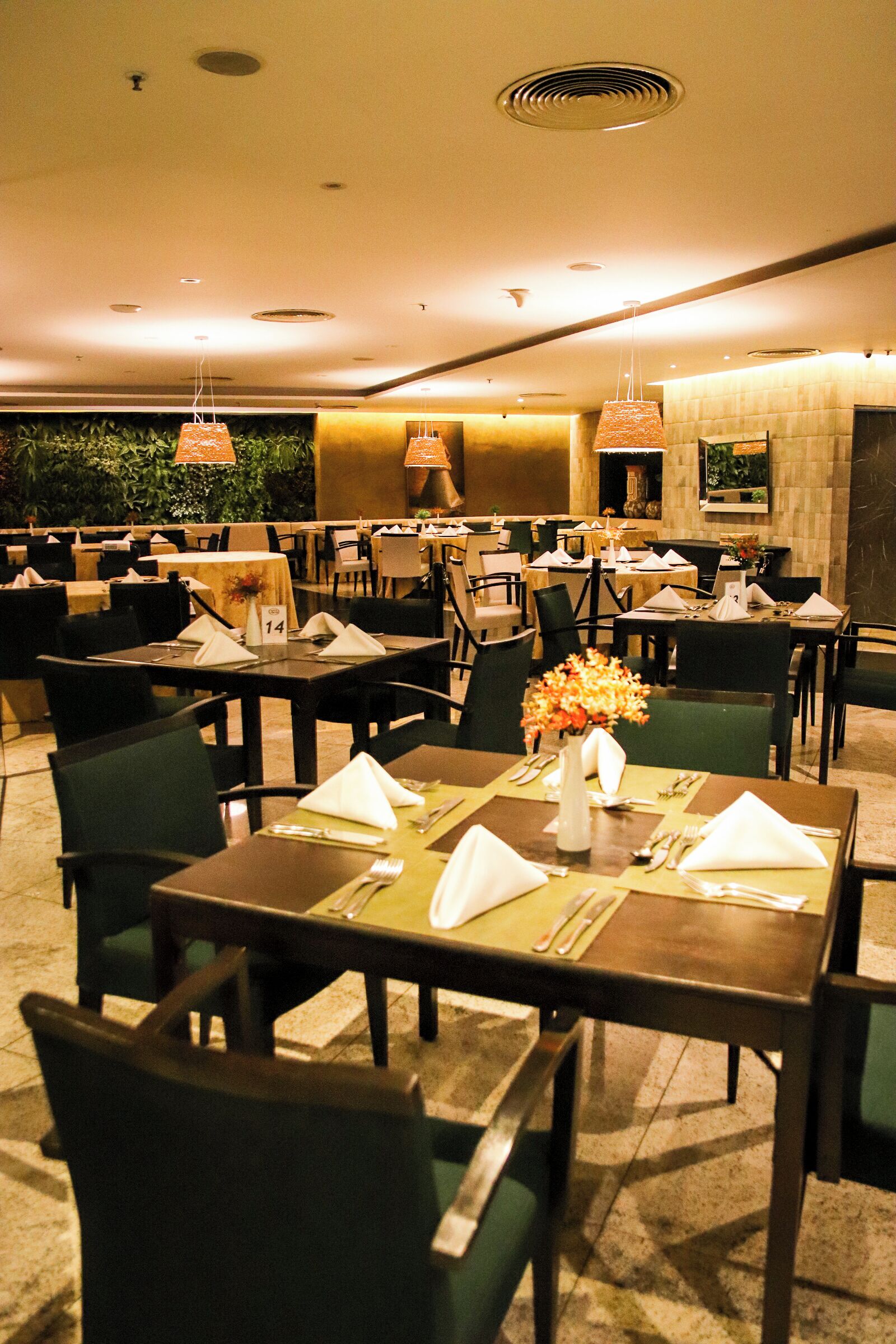 A restaurant with tables set for dining, chairs, and hanging pendant lights.