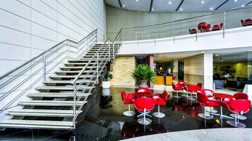 A modern hotel lobby with a central staircase, red seating area, and a reception desk.
