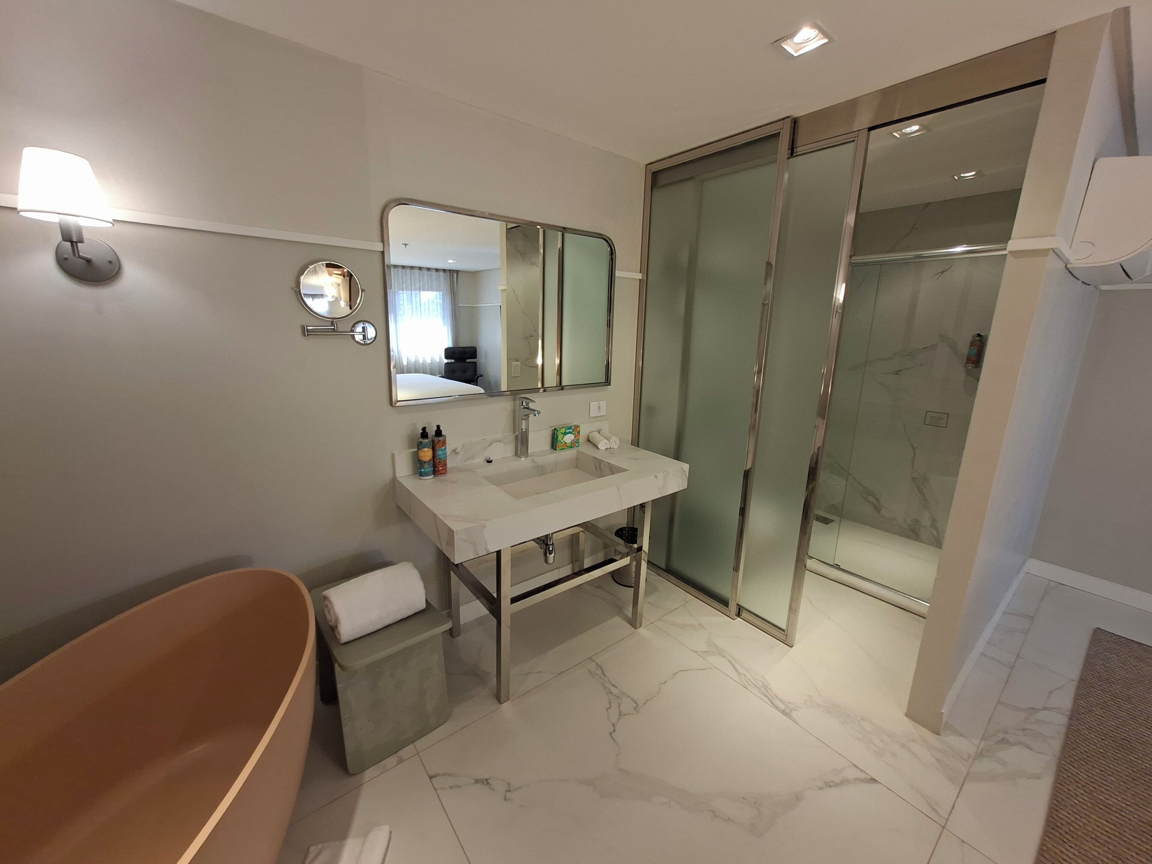 Un baño moderno con una bañera independiente, un espejo grande, un lavabo con artículos de aseo y una ducha con mampara de vidrio.