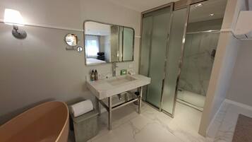 Un baño moderno con una bañera independiente, un espejo grande, un lavabo con artículos de aseo y una ducha con mampara de vidrio.