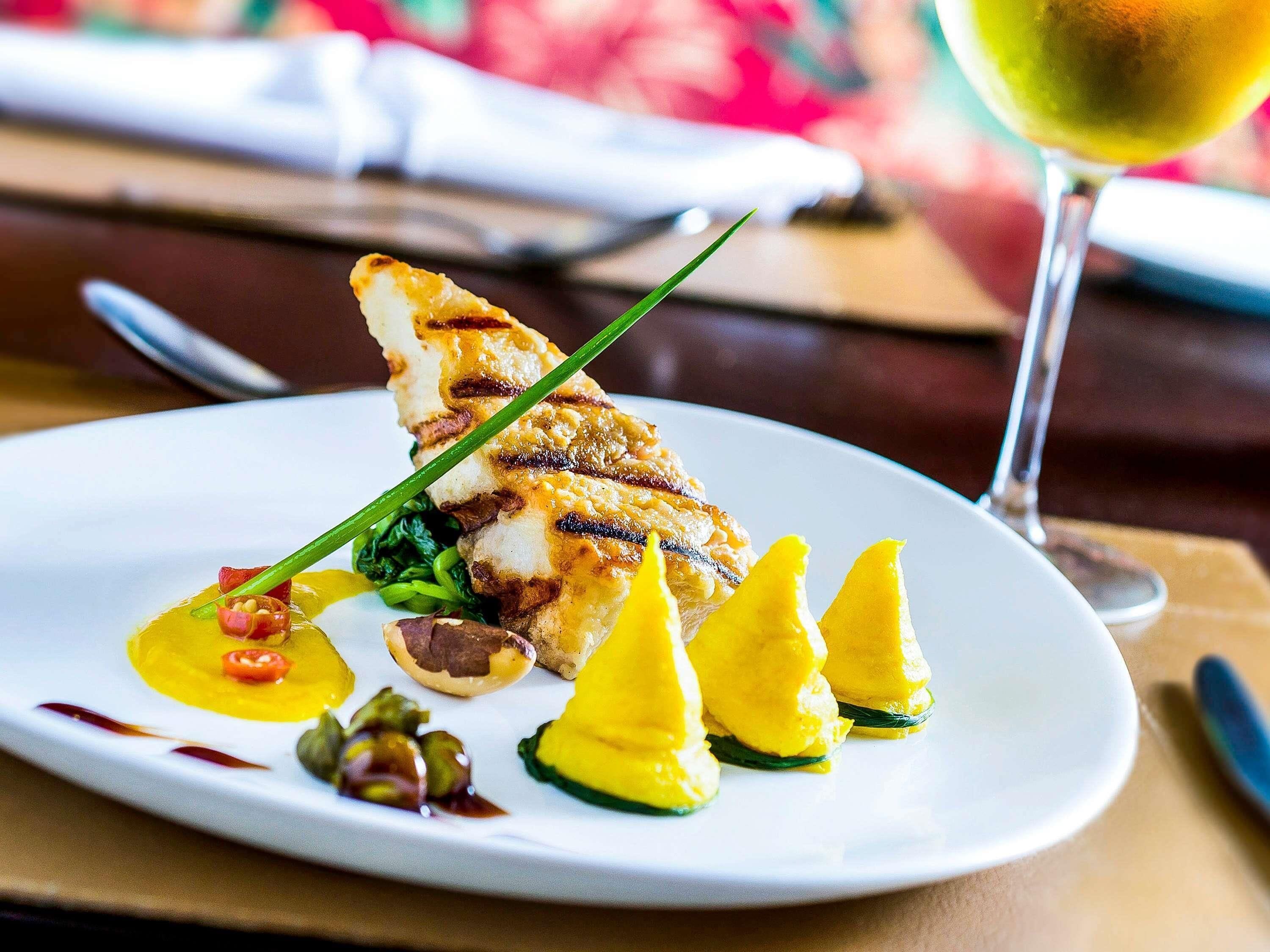 A plate of food with a grilled item, greens, and yellow elements, possibly fruit, on a white plate.
