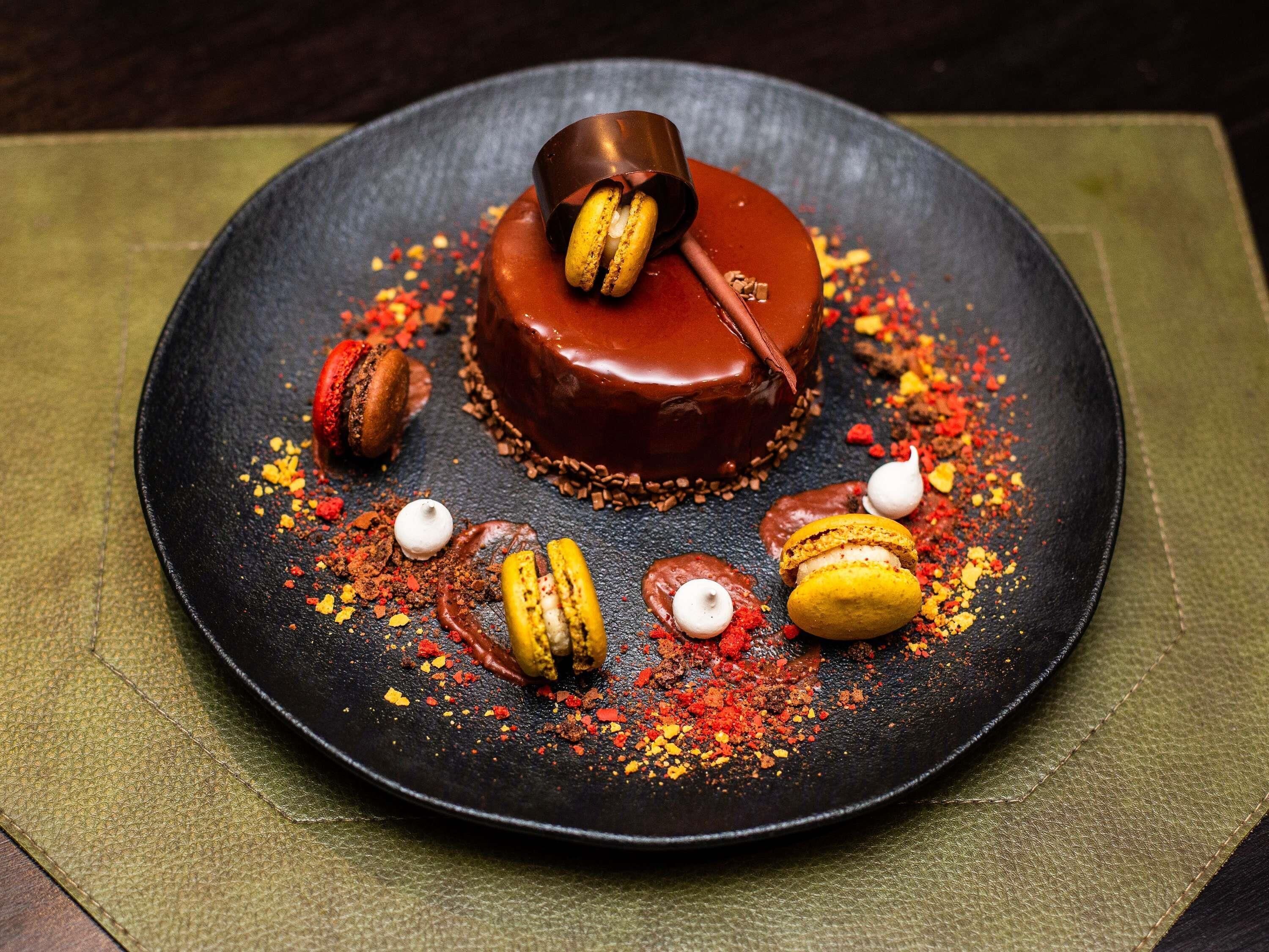 Un plato con postre, pastel de chocolate, macarons y virutas de chocolate.