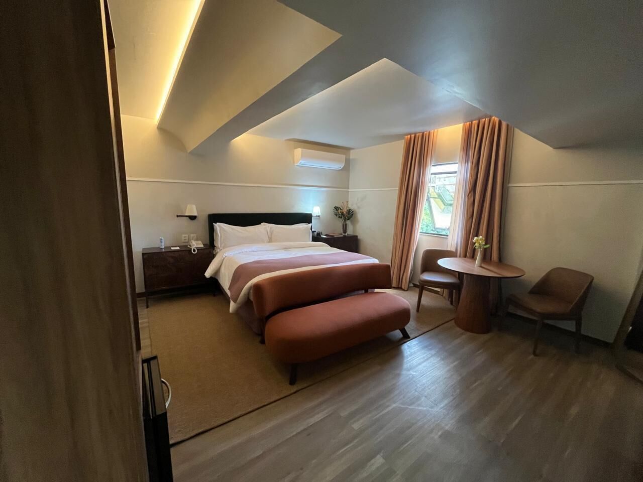 Habitación de hotel con cama, escritorio, silla, una mesita y ventana con cortinas.