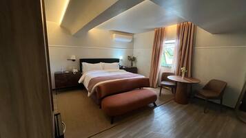 Habitación de hotel con cama, escritorio, silla, una mesita y ventana con cortinas.