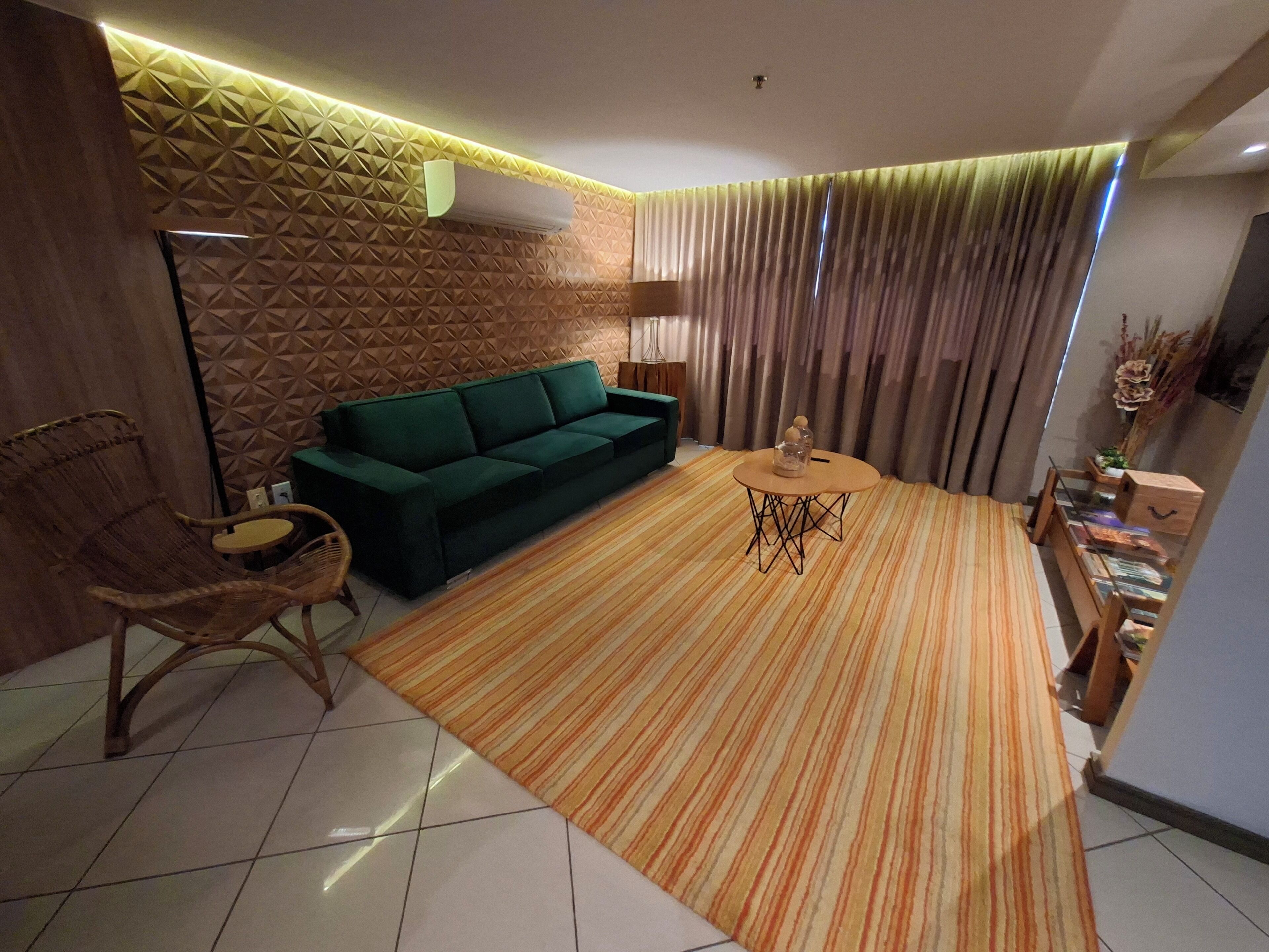 A modern living room with a green sofa, a striped rug, a wooden coffee table, and a wall with geometric patterns.