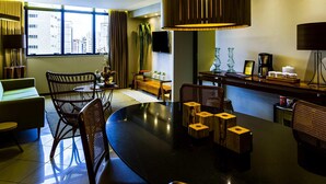 A modern living room with a round dining table, chairs, a sofa, a large window with curtains, a television, and a coffee station. - Grand Mercure Belem Do Para (Belém)