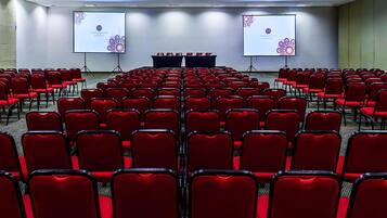 A conference room with rows of red chairs, two projection screens, and a podium at the front.