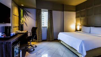 A hotel room with a bed, desk, chair, and a TV on the wall.