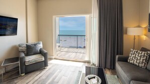 A modern living room with a sofa, a coffee table, and a view of the sea through a glass door.