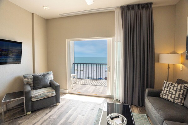 A modern living room with a sofa, a coffee table, and a view of the sea through a glass door. - Barefoot Beach Club (Madeira Beach)
