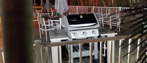 An outdoor dining area with a grill, white chairs, and umbrellas.