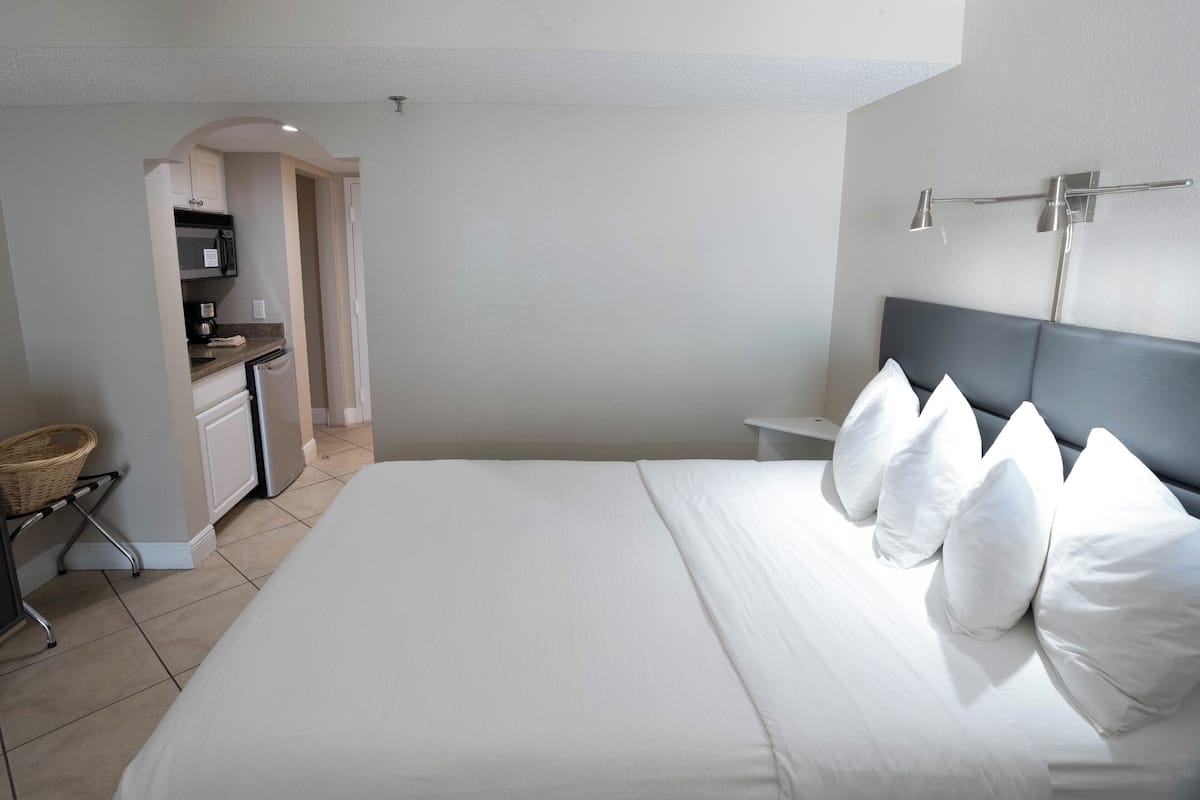 Une chambre d’hôtel comprenant un lit, une table de chevet, une lampe, une petite kitchenette et un panier.