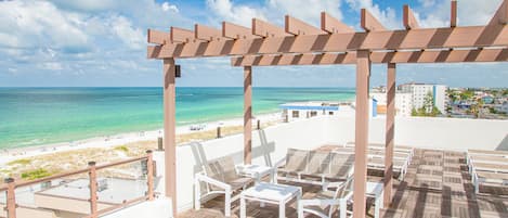 A wooden deck with lounge chairs overlooking a beach and ocean.
