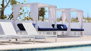 A poolside area with white canopies, lounge chairs, and a clear blue pool.