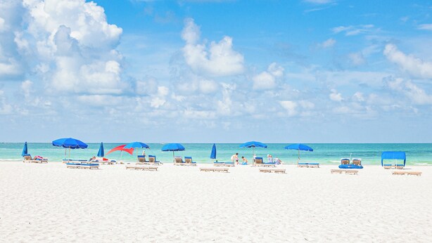 A beach with white sand, blue umbrellas, and lounge chairs.