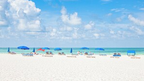 A beach with white sand, blue umbrellas, and lounge chairs. - Barefoot Beach Club (Madeira Beach)