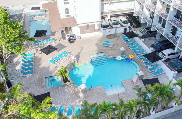 Vista aérea de un hotel con piscina, sillas de descanso y una pequeña zona de juegos.
