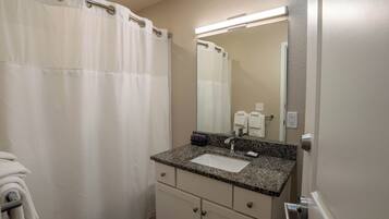 A bathroom with a white shower curtain, a sink with a granite countertop, a mirror, and a towel rack.