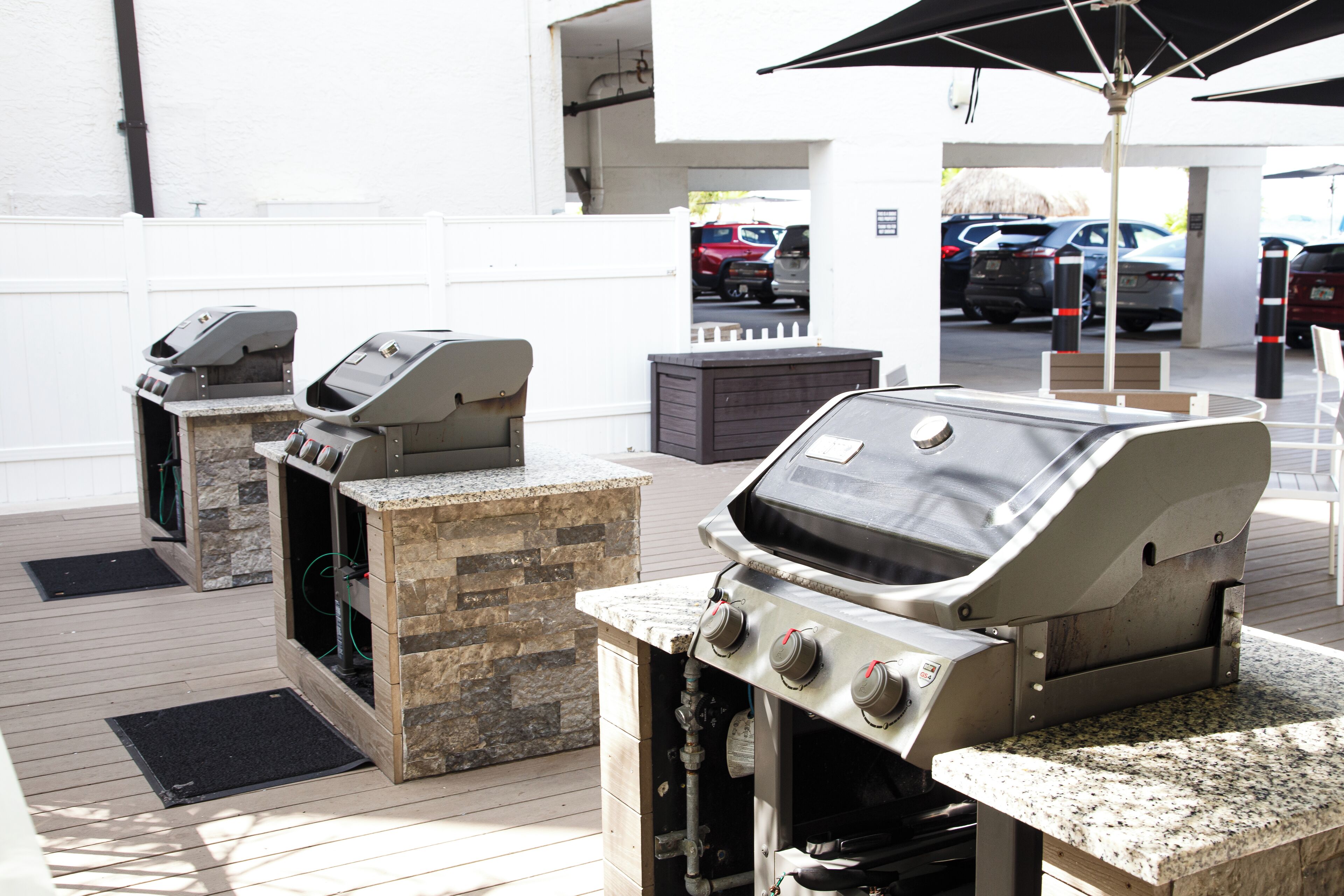 An outdoor barbecue area with two built-in grills and a gas stove, set on a wooden deck with a white fence in the background.