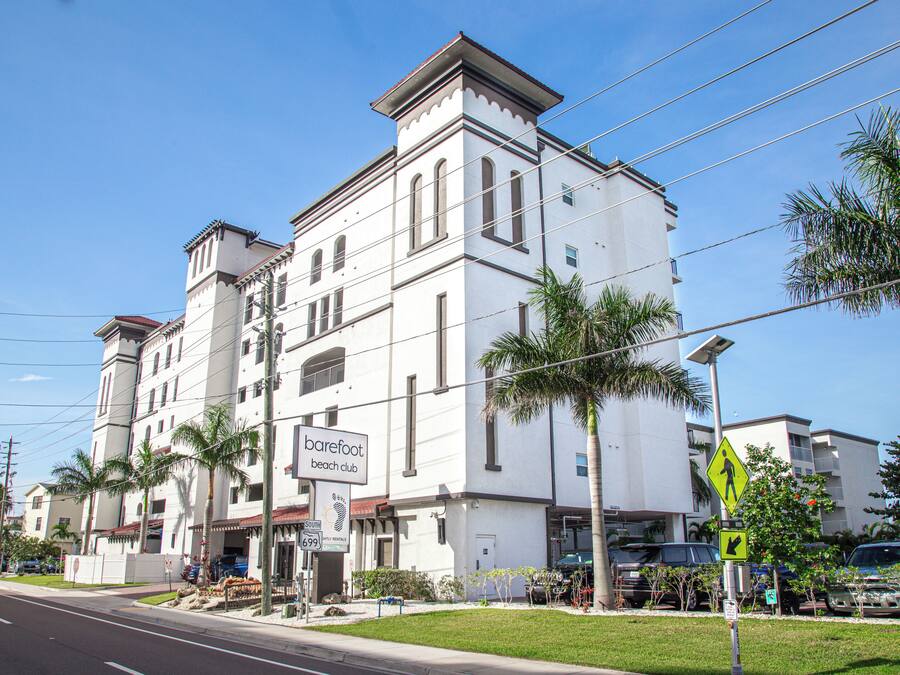 A white building with a sign for 'Barefoot Beach Club' and a pedestrian crossing sign.