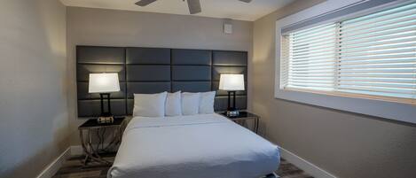 A hotel room with a large bed, two bedside tables with lamps, a ceiling fan, and a window with blinds.