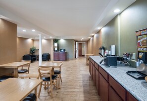 A restaurant with wooden tables and chairs, a kitchen area, and a counter with a coffee machine.