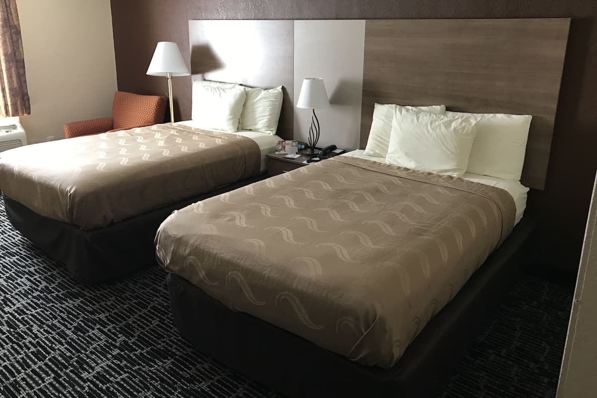 Una habitación de hotel con dos camas, una mesita de noche, una lámpara y una silla.