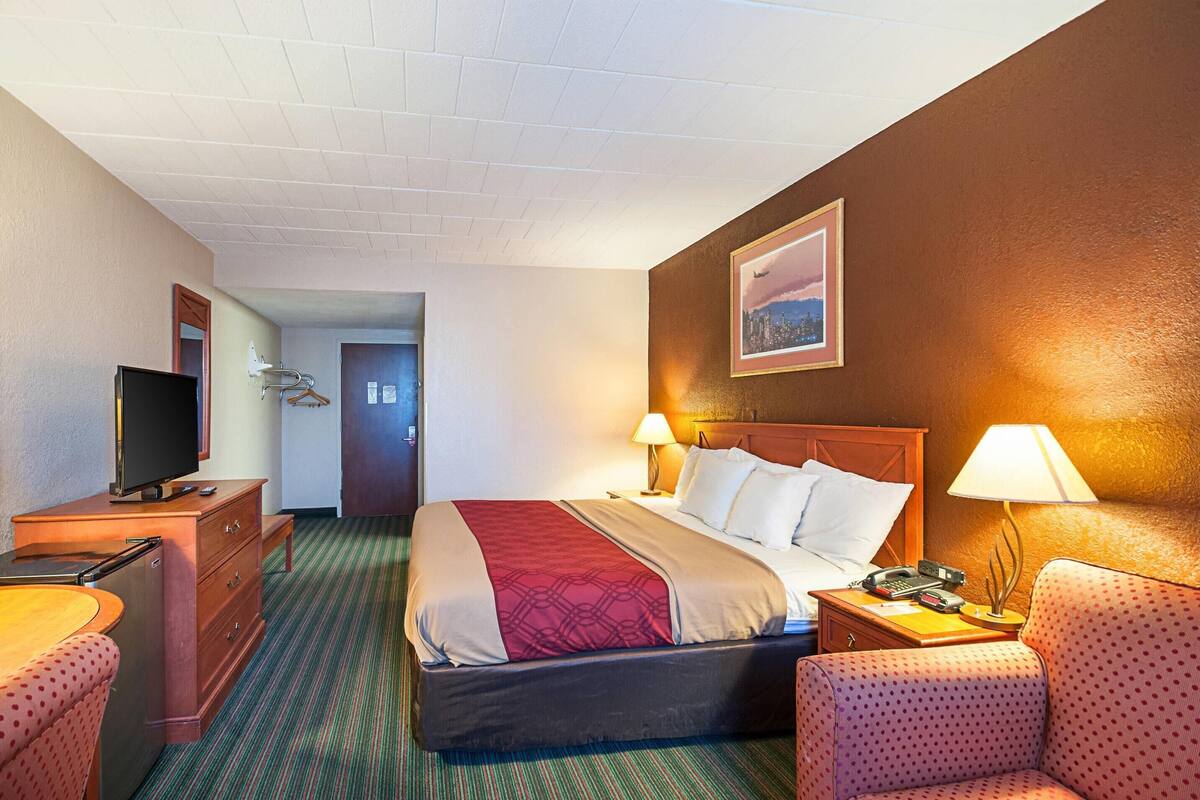 Una habitación de hotel con cama, televisión, escritorio con lámpara y una silla.