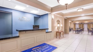Een receptiebalie met een blauwe muur, een bureau, een flatscreen televisie en een deurmat met de naam van het hotel.