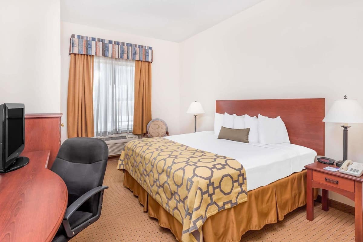 Una habitació d'hotel amb llit, escriptori, cadira, televisió i finestra amb cortines.