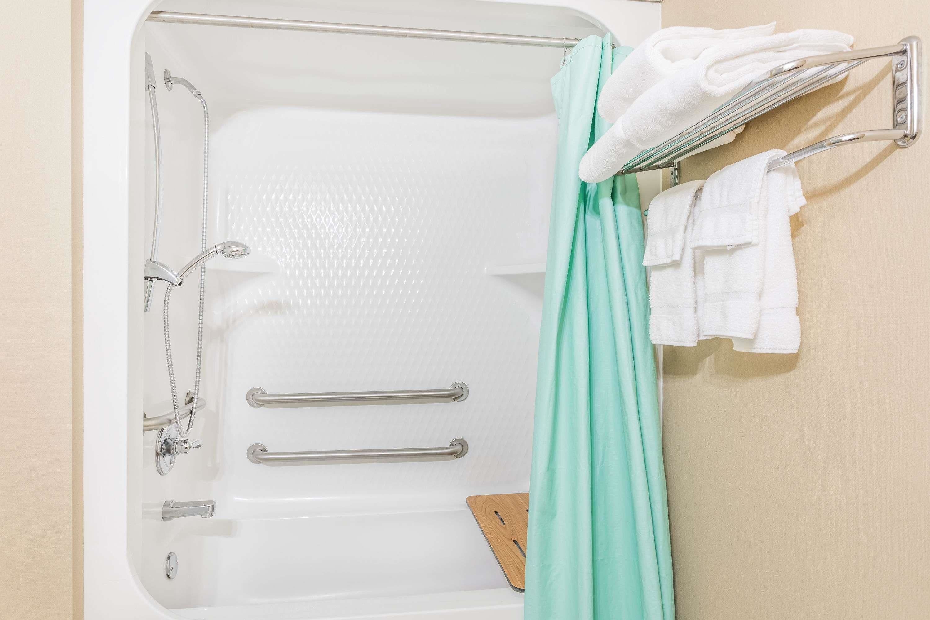 Una bañera con ducha, dos barras de apoyo y un perchero con toallas.