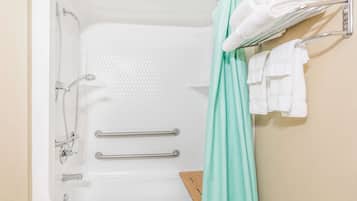 Una bañera con ducha, dos barras de apoyo y un perchero con toallas.