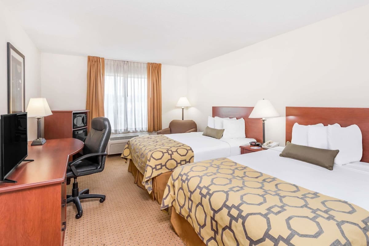 Habitació d'hotel amb dos llits, una taula amb un ordinador, una cadira, un televisor i una finestra amb cortines.