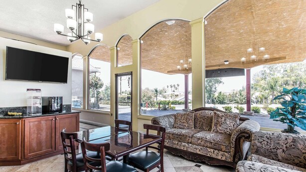 A spacious living area with a sofa, dining table, and chairs, a flat-screen TV, and a view of the outdoors. - Rodeway Inn & Suites Canyon Lake-Menifee West (Menifee)