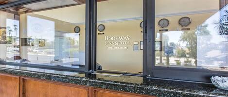 A reception area with a wooden counter, a sign for 'RODEWAY INN & SUITES' by CHOICE HOTELS, and clocks indicating different time zones.