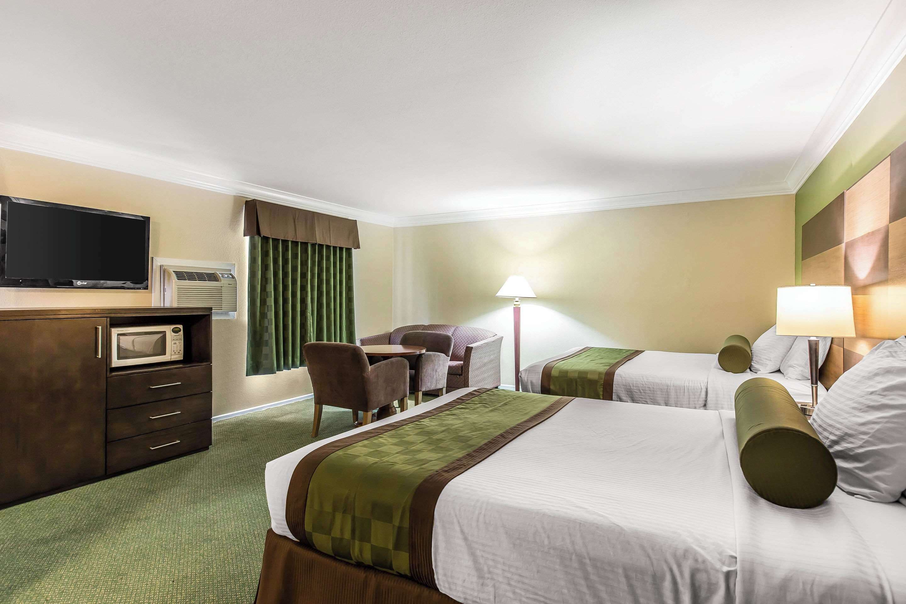 A hotel room with two beds, a desk with a microwave, a TV, a chair, and two lamps.